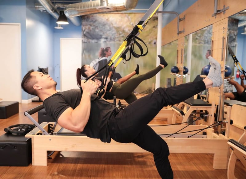 Learning from a Pilates Instructor - male member at Club Pilates doing suspension training