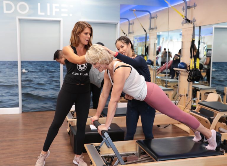 Club Pilates Instructors helping woman on a reformer machine during her class
