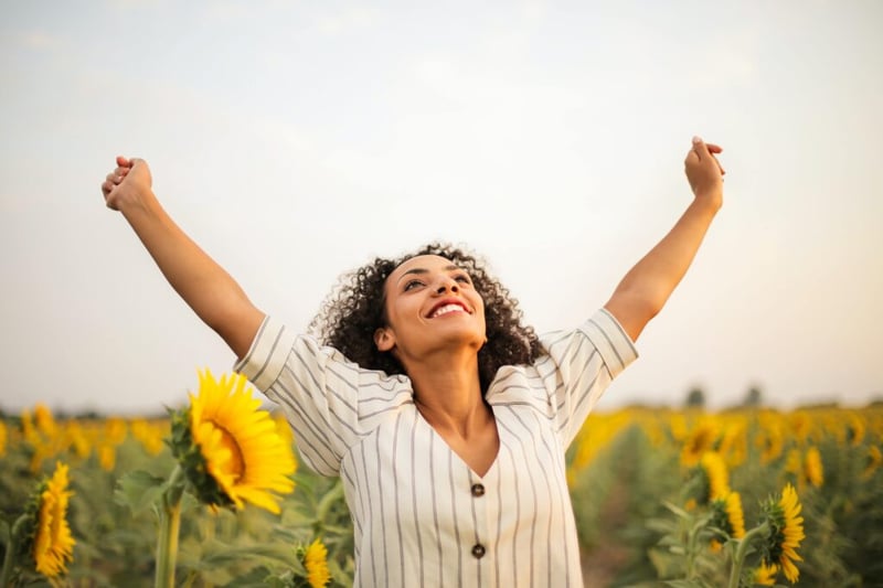 3 Ways Practicing Pilates Improves Mental Health - woman stretching arms outward in sunflower field